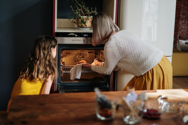 A girl watching her mother put food in the oven