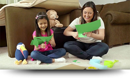 child and adult cutting green papers while seated on the floor