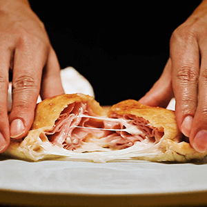 hands breaking a cheesy calzone in half